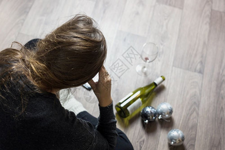 瓶子派对期望女人坐在地板上喝醉了空瓶酒在圣诞节感到沮丧圣诞球在地板上图片