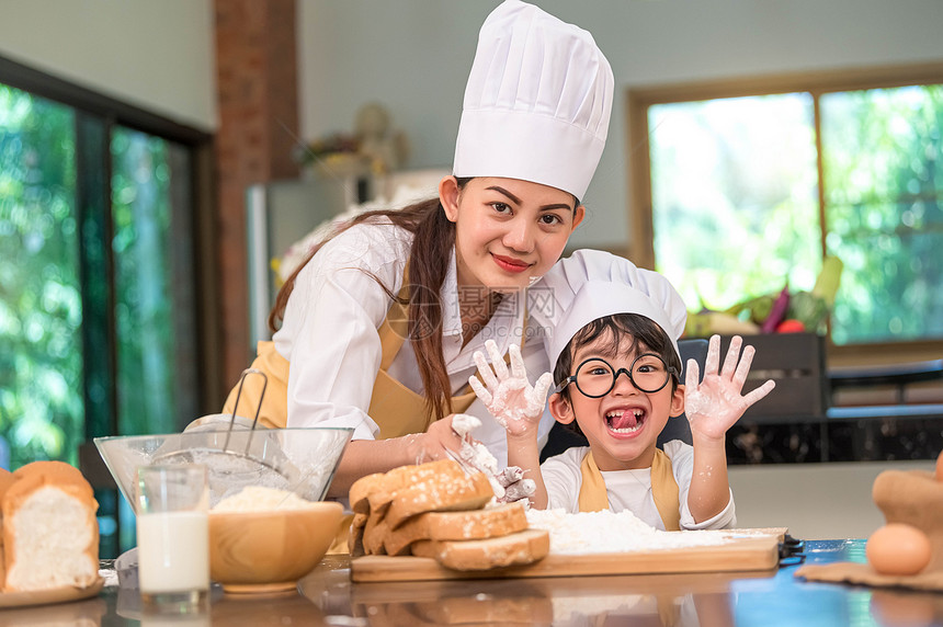 美丽的女人和可爱亚洲小男孩带着眼镜厨帽和围裙在家中厨房里玩烘烤面包店有趣的概念是自制食物和面包有趣的部情调看着相机家庭微笑制造图片