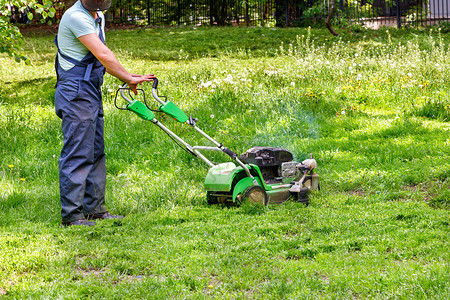 用工荒公园穿蓝衣的用工人照顾绿草坪使用汽油割草机身穿蓝服的工人用业油采草机砍伐绿城市的剪机背景