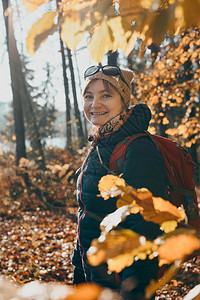 中间冒险旅游在秋天阳光明媚的白带着背包在森林里游荡的女人露天阳光晴朗的夜晚站在中年活跃女视野前积极花着闲暇时间走在林道上树木间有活动高清图片素材