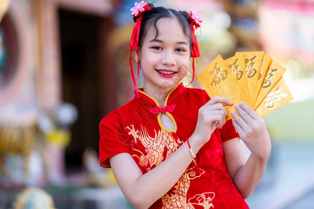 穿着红色传统青山装饰的可爱小亚洲女孩肖像拿着黄信封上面写着中文字祝福是新年节的幸运日啊中华新年节的钱黄色背景图片