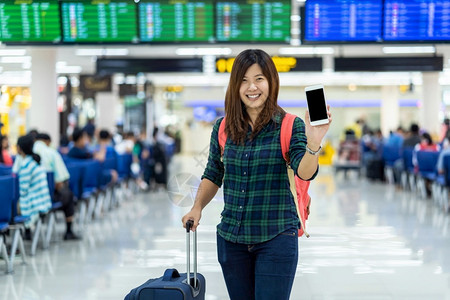 亚洲旅行者携带李在现代机场飞行信息屏幕的带有技术概念的旅行和运输上显示智能移动电话以登入飞行板的亚洲旅者和及运输工具挤移动的亚洲日程高清图片素材