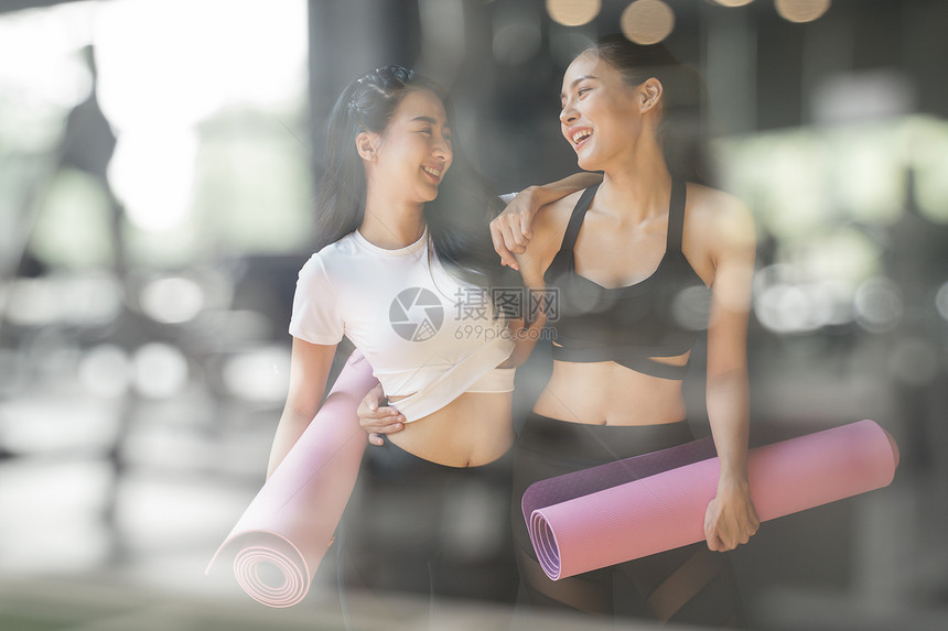 一个十几岁女孩朋友在体育馆的模糊前景上放弃瑜伽后正在步行坐紫色瑜伽垫上照片来自一个亚洲年轻女子的玻璃窗在健身设施里聊天和嘲笑紫色图片