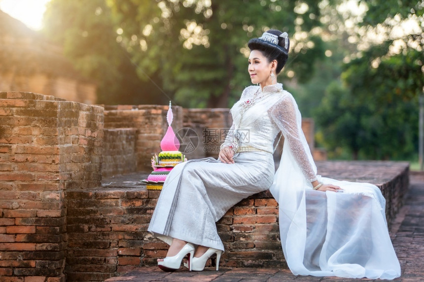 身着泰国白色传统服装穿着Krathoong和坐在泰国古老城市塔寺门前的Trathong妇女LoyKrathong节Transge图片