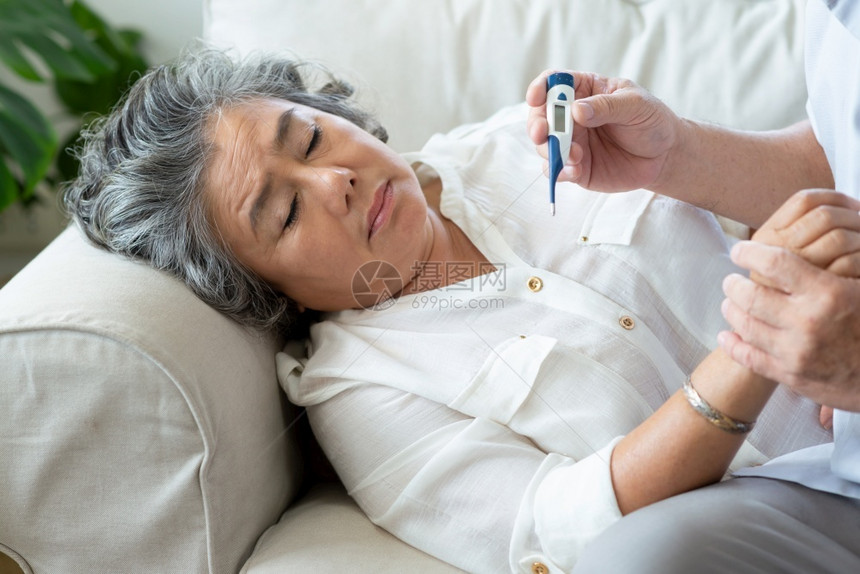 泰国不适年长妇女在沙发上躺着寒冷而年长男子在家中用数字温度计检查其妻子的温度时睡在沙发上有烧病疾科罗纳毒Covid扩散检疫car图片