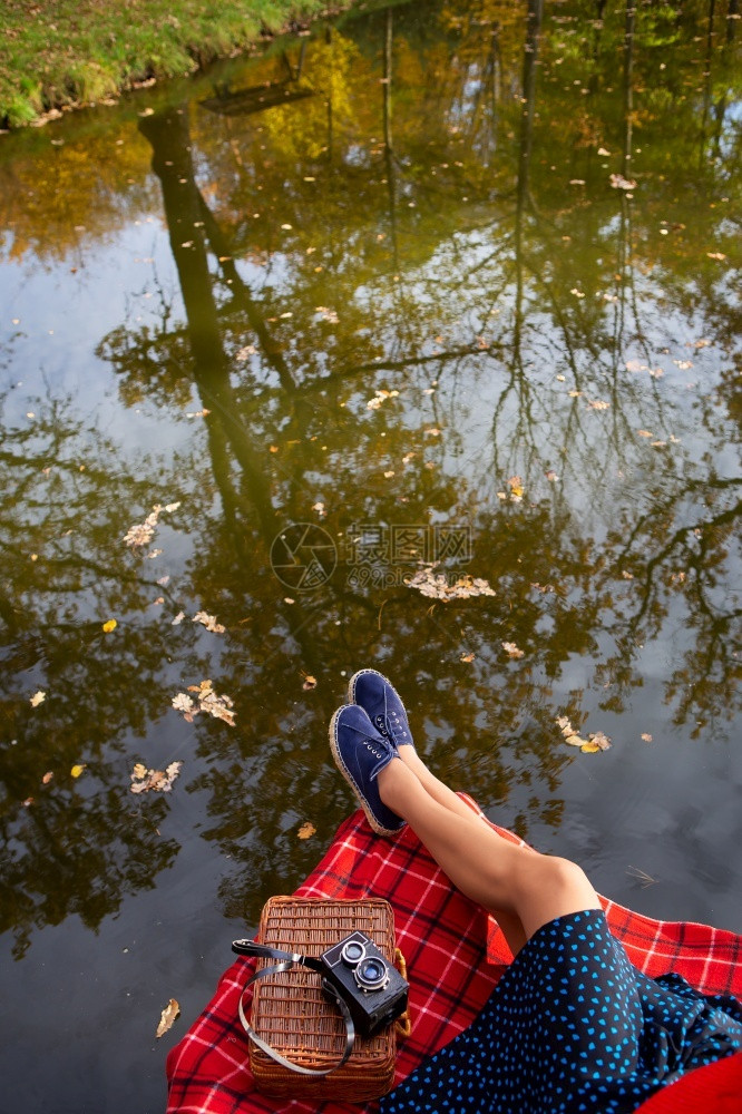 湖边一个小女孩的腿躺在红色格子上水中美丽的倒影水面上落叶从方看湖边一个年轻女孩的腿在红色笼子里的格上水中美丽的倒影从上面天思维靠图片