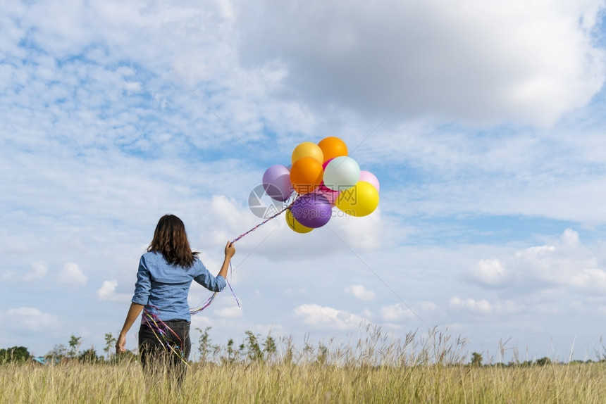 美丽的女人拿着气球在绿色草地白云和蓝天空上奔跑快乐轻松的天空手拿着充满活力的空气球在生日派对上欢快的盛宴玩束可爱的图片