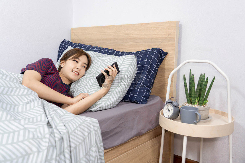 放松每天日常概念一名女青少年在睡觉前用她的智能手机进入床上敲响报警器的日常概念打盹环境图片
