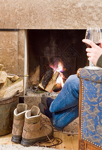 休息咝作响男人在壁炉边用一杯红酒放松在长途远走之后他的靴子在旁边暖和起来热篝火高清图片素材