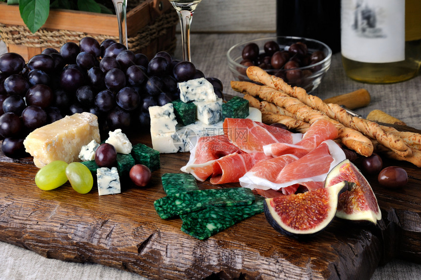 熏肉猪木板上的安提帕斯托Antipasto配有香菜不同种类的奶酪葡萄和无花果子图片