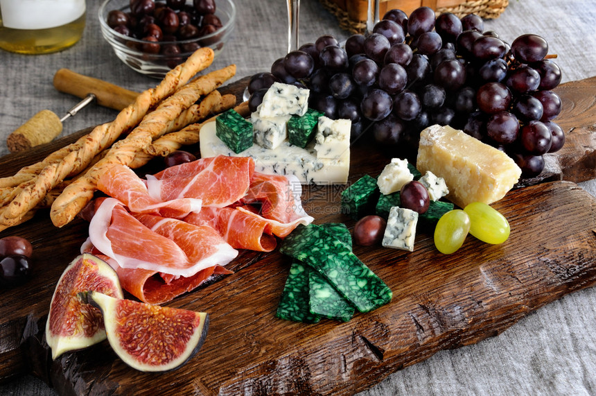 木板上的安提帕斯托Antipasto配有香菜不同种类的奶酪葡萄和无花果子吃帕尔马生涩的图片