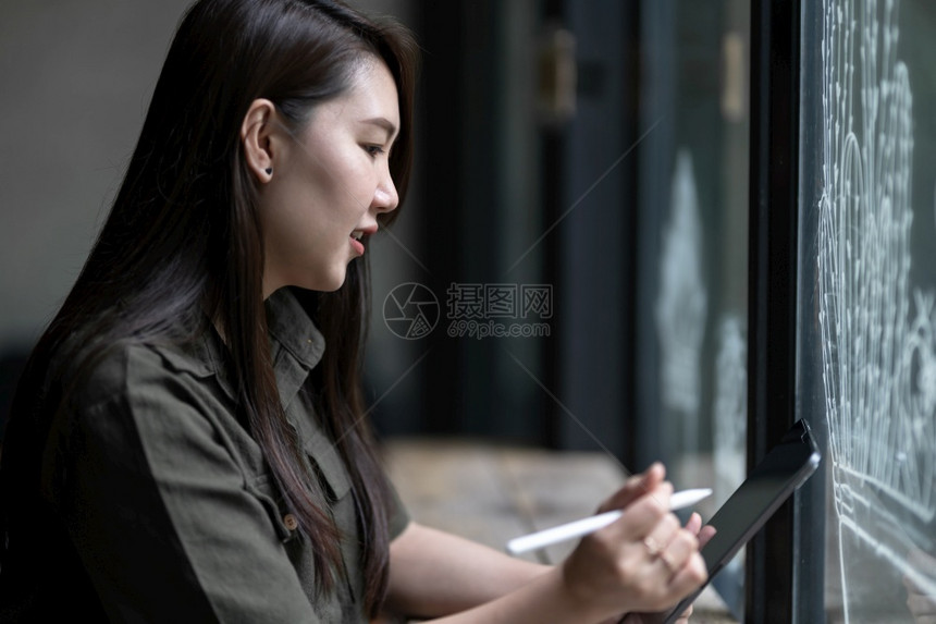 沟通在数字平板电脑上工作的女临时注意咖啡店厅背景中穿着棕褐色绿衣时装髦的电子笔纸牌吸引人的商业图片