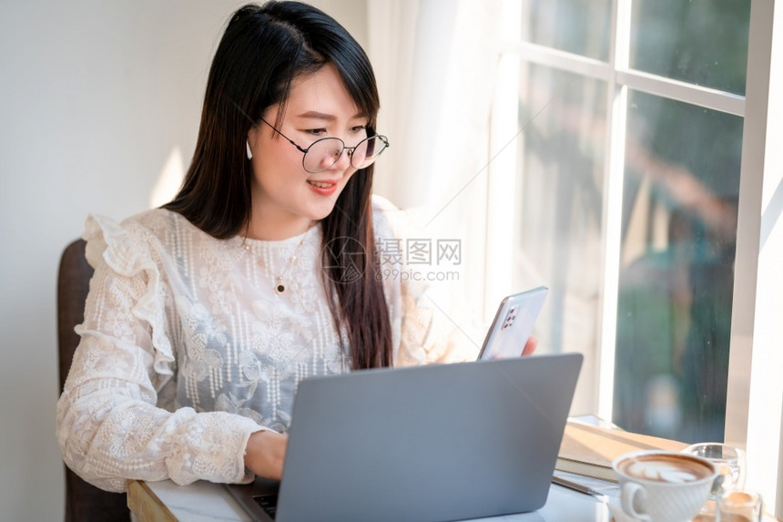 吸引人的商业女在智能手机上写信息并举行咖啡杯茶在咖啡馆商务生活方式用笔记本电脑工作的闲电话在线的图片