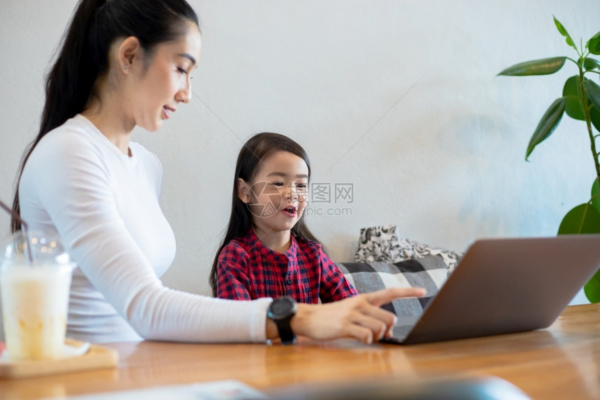 爱活的亚洲母亲正在教女儿阅读一本书并使用笔记本和技术在家庭学校放假期间进行网上学习教育概念和家庭活动教育概念与家庭活动利用笔记及图片