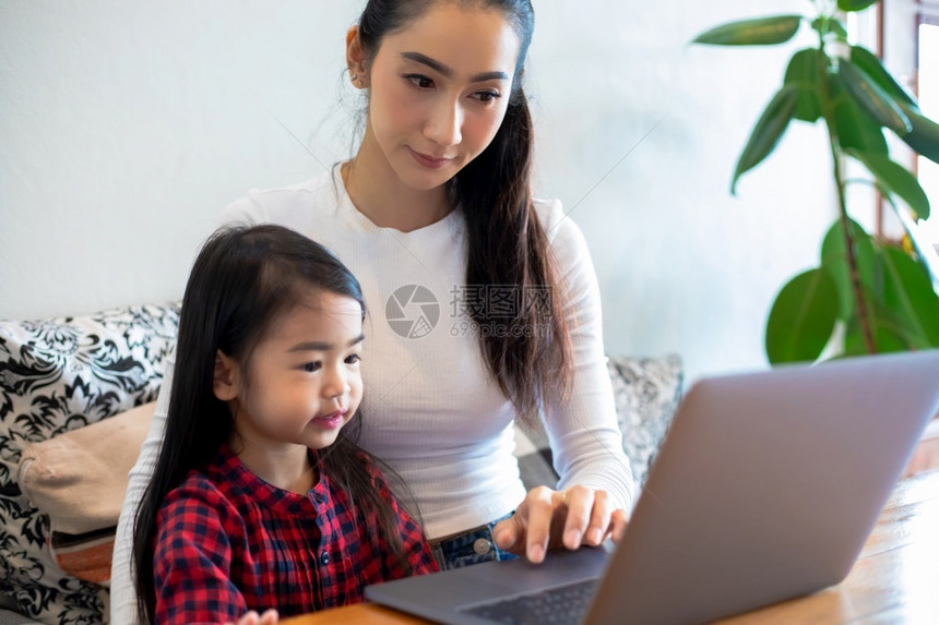 美丽的亚洲母亲正在教女儿阅读一本书并使用笔记本和技术在家庭学校放假期间进行网上学习教育概念和家庭活动教育概念与家庭活动利用笔记及图片