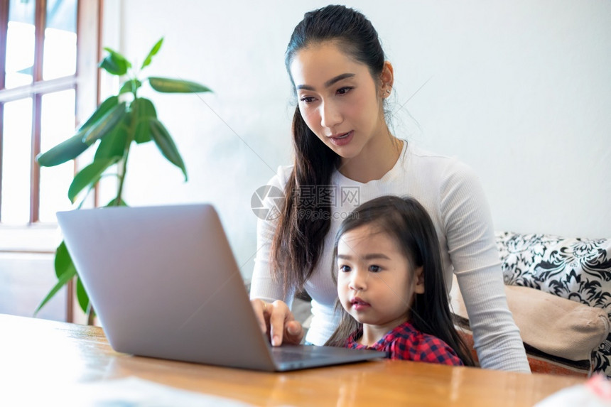 坐着亚洲母亲正在教女儿阅读一本书并使用笔记本和技术在家庭学校放假期间进行网上学习教育概念和家庭活动教育概念与家庭活动利用笔记及技图片