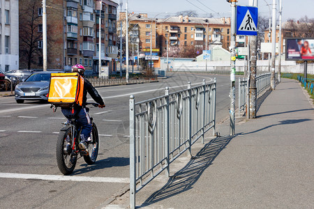 沿着一个人在条城市街道人行的公路上骑电动自行车这是动自由的现代概念一名背着橙色的年轻人正在一座城市街道沥青路旁骑电动自行车晴天未圆形的高清图片素材