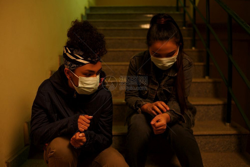 担心污染身着一次医疗保护面罩的亚洲和非少女年轻孩坐在楼梯井里有选择地重点救助在跨种族国际援助友谊下从感染中拯救出来楼梯间图片