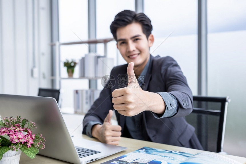 男人技术年轻的青商人在笔记本电脑上看到一个成功的商业计划文件论抽象摘要的焦点模糊显示办公室木制桌背景上的拇指和在办公室内用木制桌图片