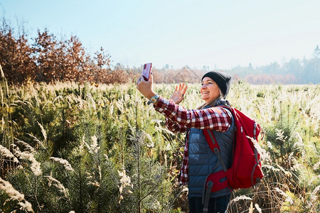 挥手致别女在视频电话中挥舞在山上度假旅行时致问候女背包徒步穿过高草地沿着的路走过渡与自然相亲的暑假漫游期幸福背景