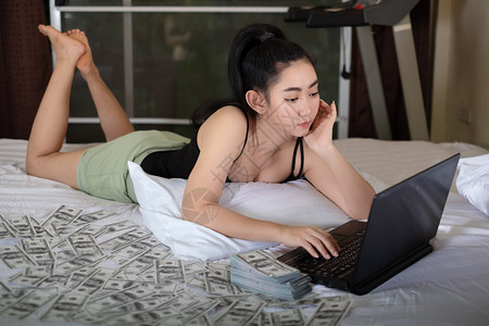 躺在床上卧室的笔记本电脑上工作里面有10美元的钞票很多来自家概念的作品以盈利为目的卖商品SellProfessionalsfor女士高清图片素材