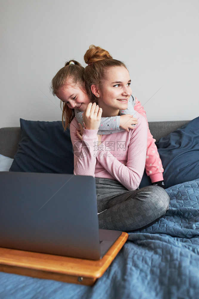 家庭在COVID19检疫期间女孩和她的妹一起在家里用笔记本电脑学习女孩们坐在计算机前的床上女孩们坐在电脑前人室内图片
