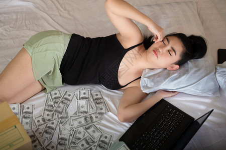 困穿着笔记本和10美元钞票睡在卧室的床上亚洲年轻有魅力的肖像女青年很多是自家作品卖商以牟利概念SellProjectsfor盈利小憩高清图片素材