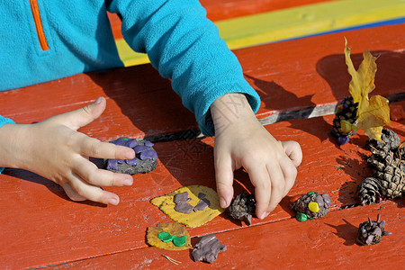 项目各种样的孩子在户外玩耍图片是小孩子在红木书桌后面的街道上玩橡皮泥一个孩子在玩粘土和各种形状不同的天然材料毛衣玩具高清图片素材