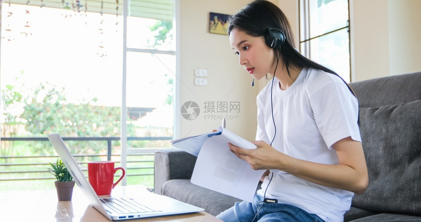 女孩亚裔快乐学生在网上观看络研讨会播客在笔记式学习教育课程会议上观看网络研讨会播客电话和写笔记看膝上型电脑坐在家中沙发上亚洲公寓图片