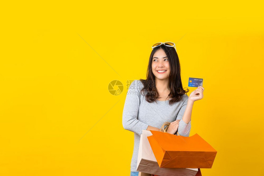 黄色的女孩情绪化快乐亚洲微笑女使用信卡并携带一个购物大包装袋在孤立的黄色背景复制空间和工作室黑色周五销售上展示网购物同时提供黑星图片