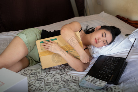 情绪说谎穿着笔记本和10美元钞票睡在卧室的床上亚洲年轻有魅力的肖像女青年很多是自家作品卖商以牟利概念SellProjectsfo情感高清图片素材
