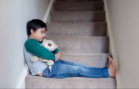 暴力情绪化的独自坐在楼梯上与泰迪熊同坐的萨德阿西安男孩带着悲伤的脸看哀孤独孩子不高兴回到学校沮丧的男孩坐在楼梯角落里家庭哭高清图片素材
