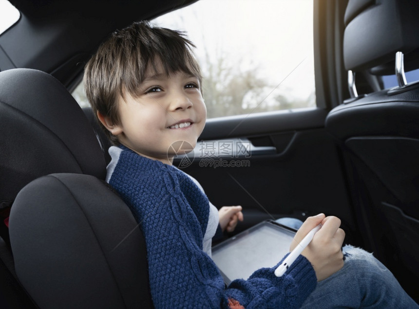 假期童年幸福快乐的男孩在坐带有安全的汽车后座乘客位上时使用平板电脑儿童男孩靠智能垫子画幼儿长者肖像在公路旅行中自娱乐己图片