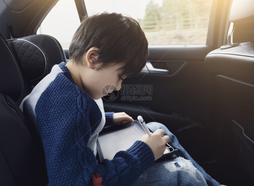 学步的儿童快乐男孩在坐带有安全的汽车后座乘客位上时使用平板电脑儿童男孩靠智能垫子画幼儿长者肖像在公路旅行中自娱乐己腰带玩图片