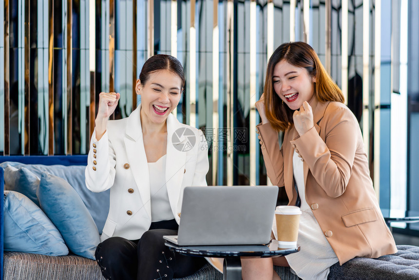 两个亚洲女企业家在通过现代办公室或合用空间咖啡休息和下班后谈话的技术笔记本电脑检查成功目标时一起欢庆两个亚裔女实业家工作场所成功图片