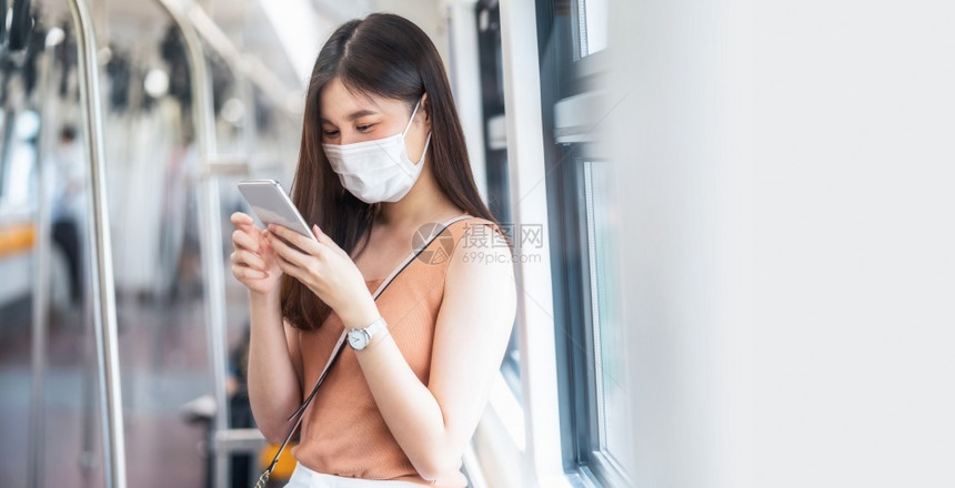 在Covid19爆发感染和大流行病概念的都市旅行时身戴外科面具并通过地铁火车智能手机监听音乐的亚洲女青年乘客在Covid19爆发图片