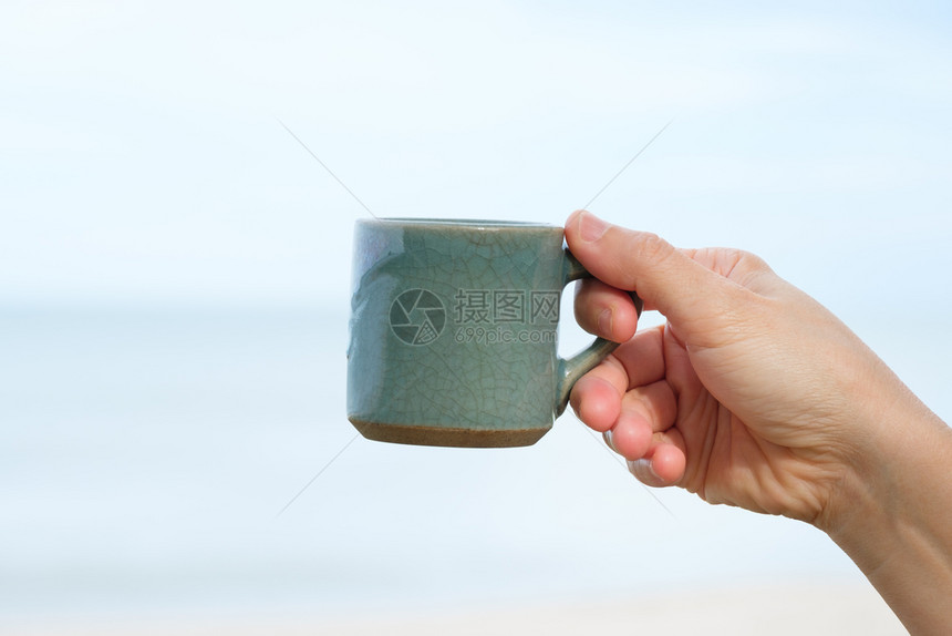 手指喝陶瓷制品握在海和天空背景上带着和平喜悦的概念用手举着陶瓷杯咖啡图片