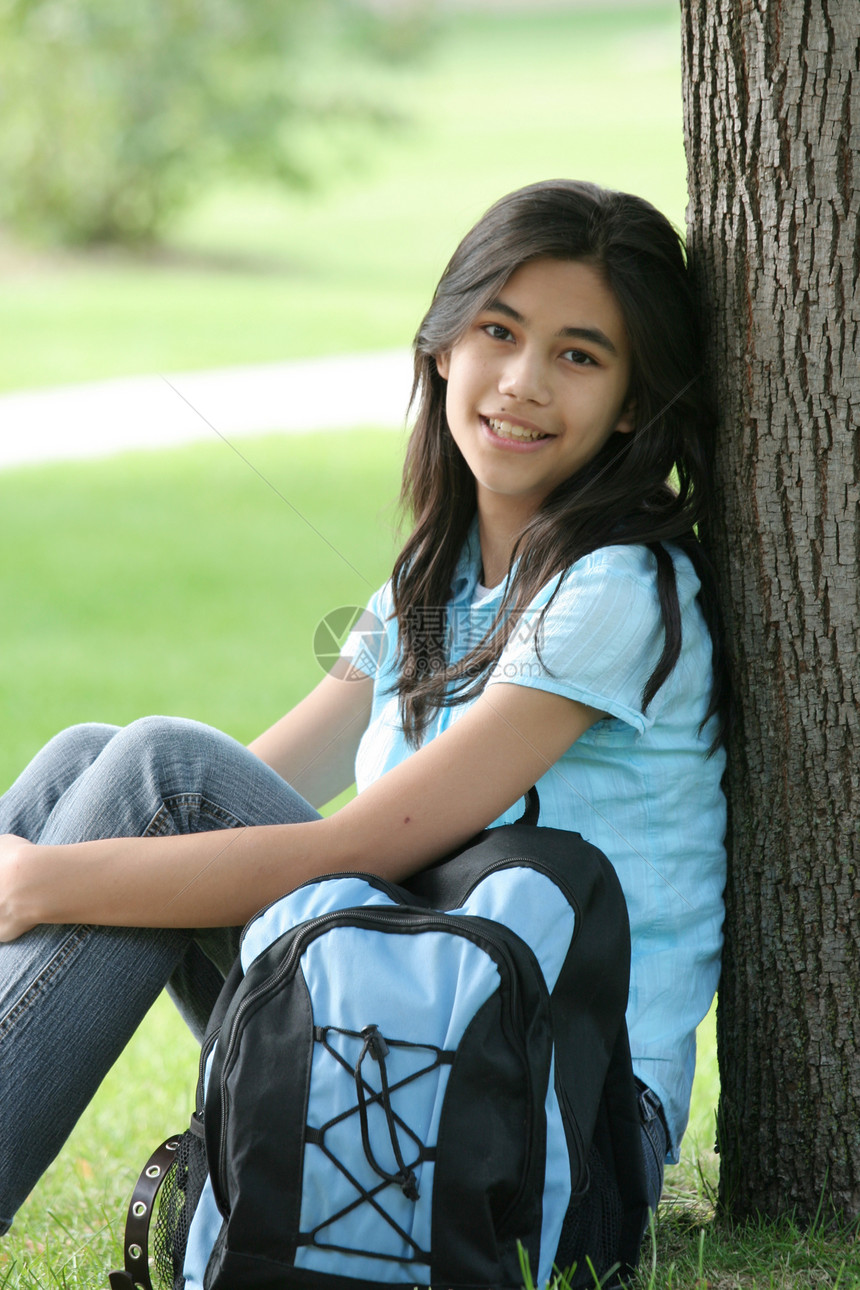 年轻女孩坐在树边 背着背包中学青少年公园学生孩子草地微笑混血图片