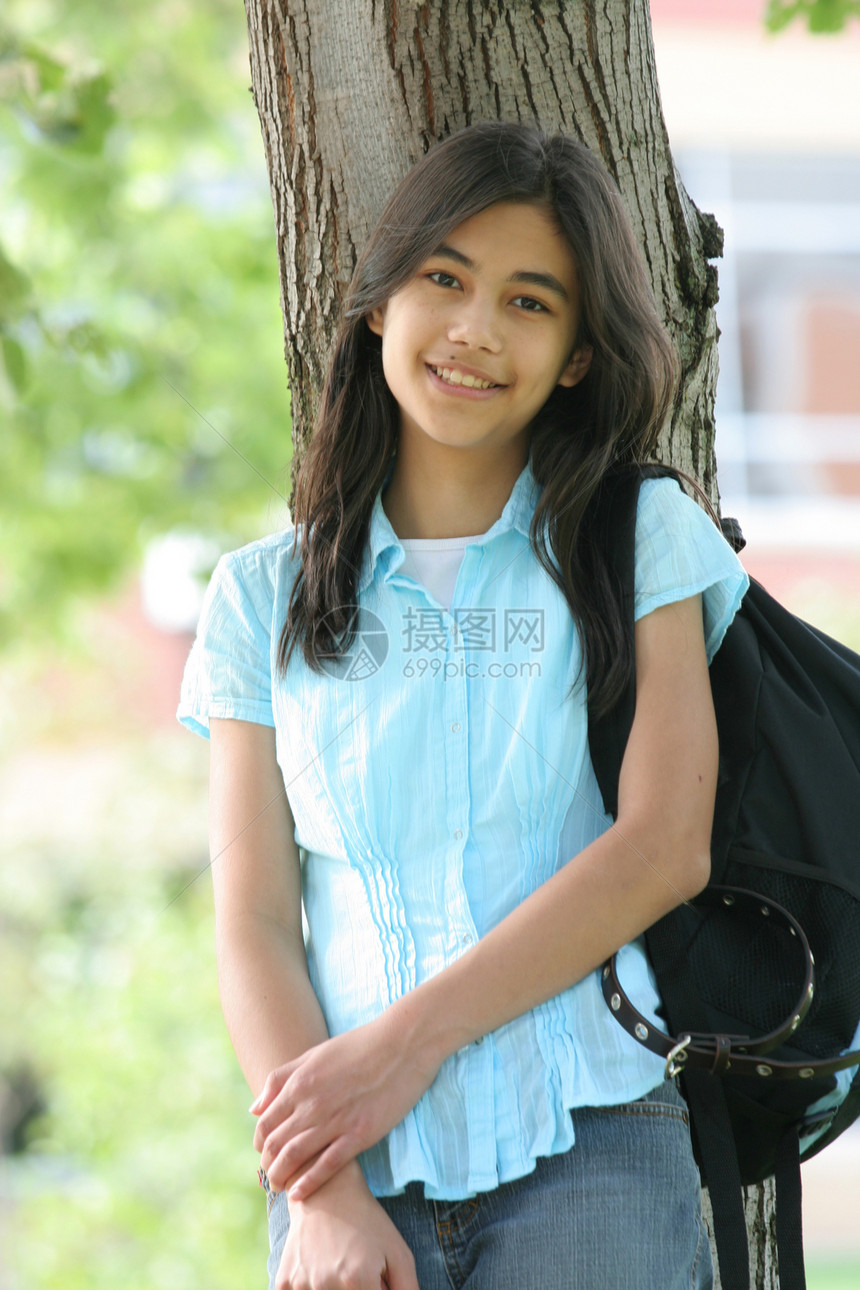 年轻女孩带着背包站在树上 微笑着精力晴天中学学生青少年混血孩子图片