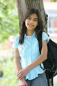 年轻女孩带着背包站在树上 微笑着精力晴天中学学生青少年混血孩子背景图片