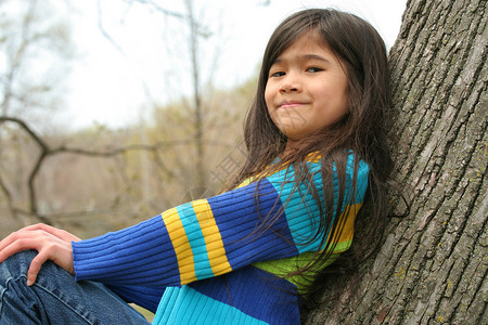 坐在树上可爱的小女孩微笑混血精力牛仔裤女性福利孩子倾斜背景图片