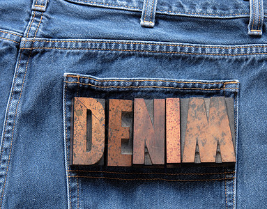 隐性印刷首都字母牛仔裤织物蓝色口袋墨染木头棕色背景图片