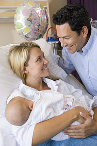 新母亲带着婴儿和丈夫在医院中微笑的笑容新妈妈访问家长拥抱拜访男性女性气球妈妈女士父亲高清图片素材