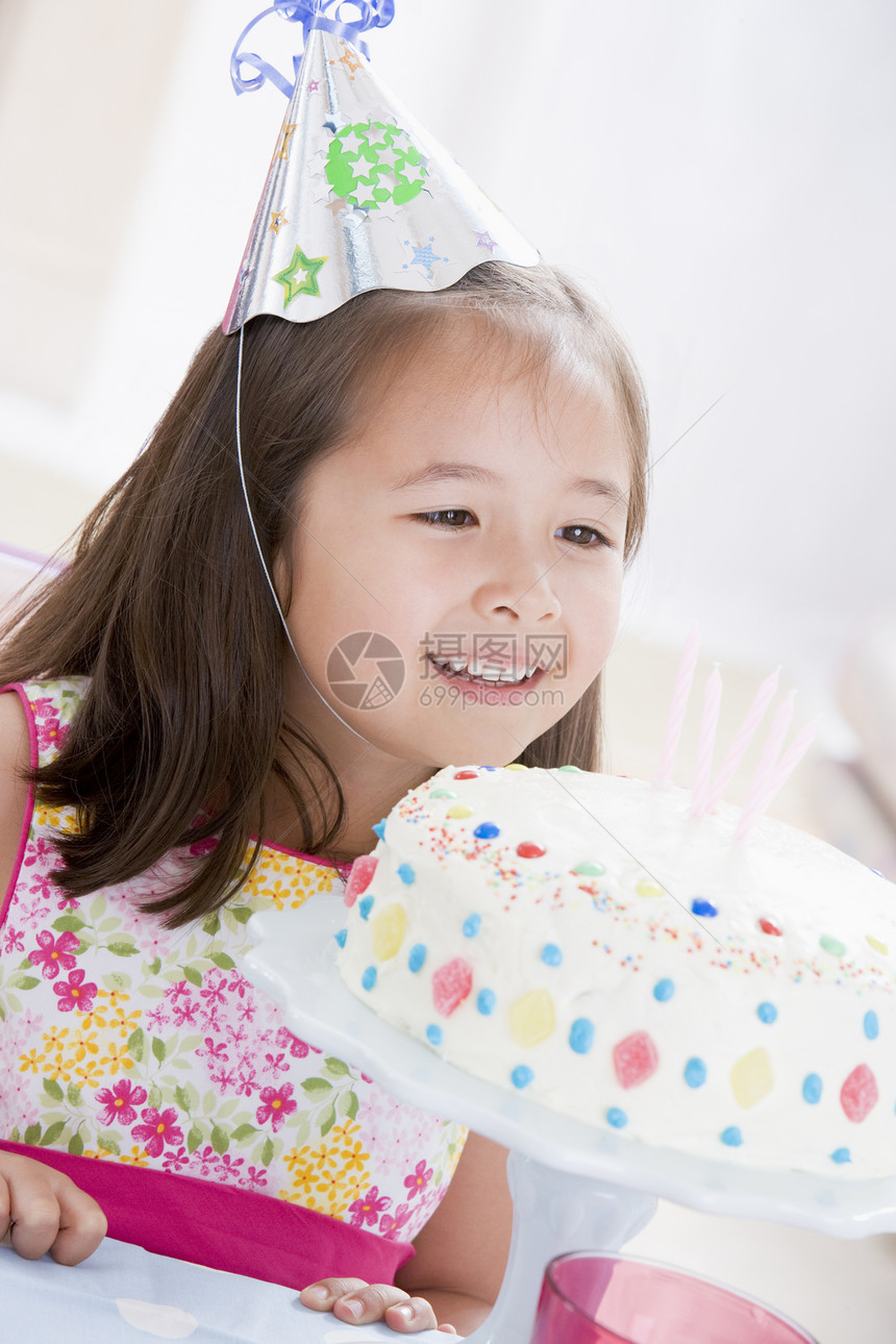 戴着党帽的年轻女孩 看着生日蛋糕微笑着笑蜡烛派对女性生日桌子孩子们孩子食物混血图片