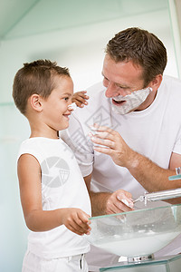上洗手间男孩男人在洗手间 在男孩鼻子上涂剃须霜背景