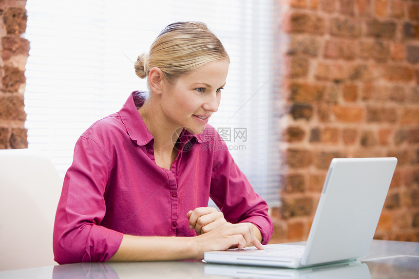 利用手持笔记本电脑微笑坐在办公室的女商务人士图片
