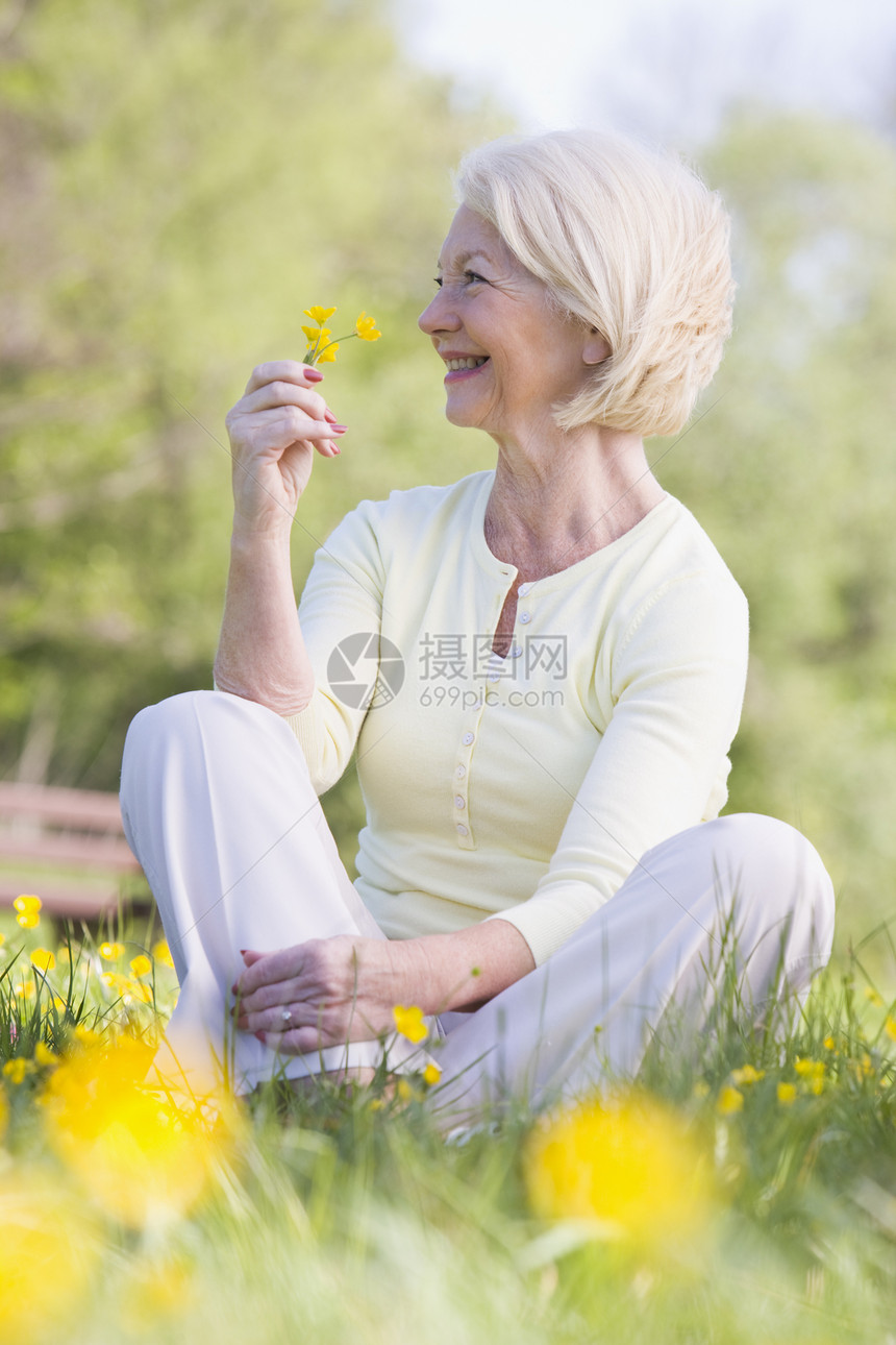 女人坐在户外微笑着笑着 拿着一朵 Buttcup花野花公园女性农村采摘女士场地花朵退休毛茛图片