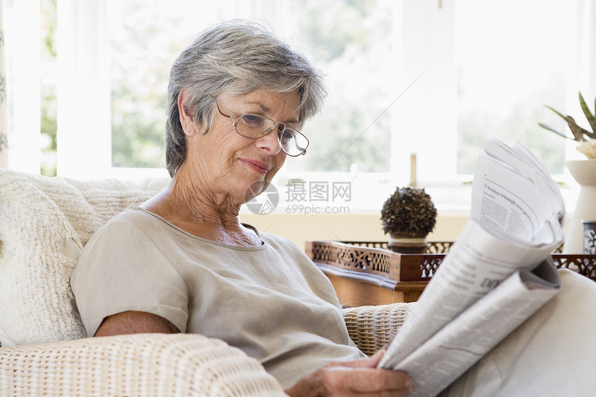 上客厅看报纸的妇女沙发退休休息室微笑女士水平长椅女性阅读眼镜图片
