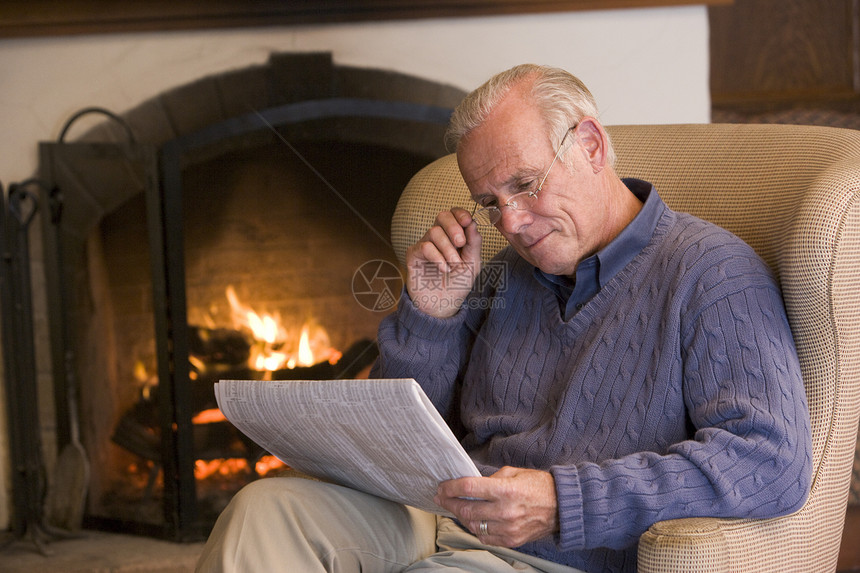 坐在起居室的男子与报纸在壁炉旁边图片