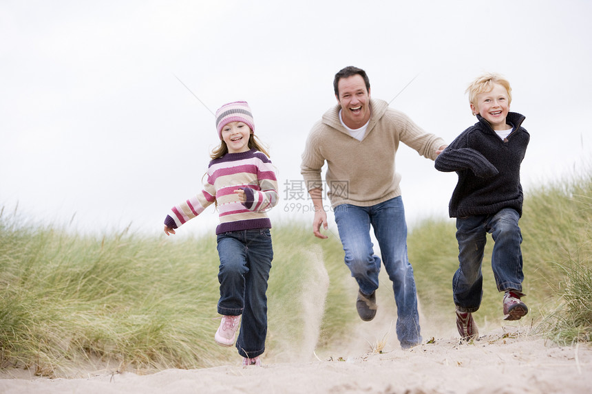 父亲和两个小孩在海滩上笑着跑季节相机微笑自由踪迹孩子们跑步享受视角途径图片